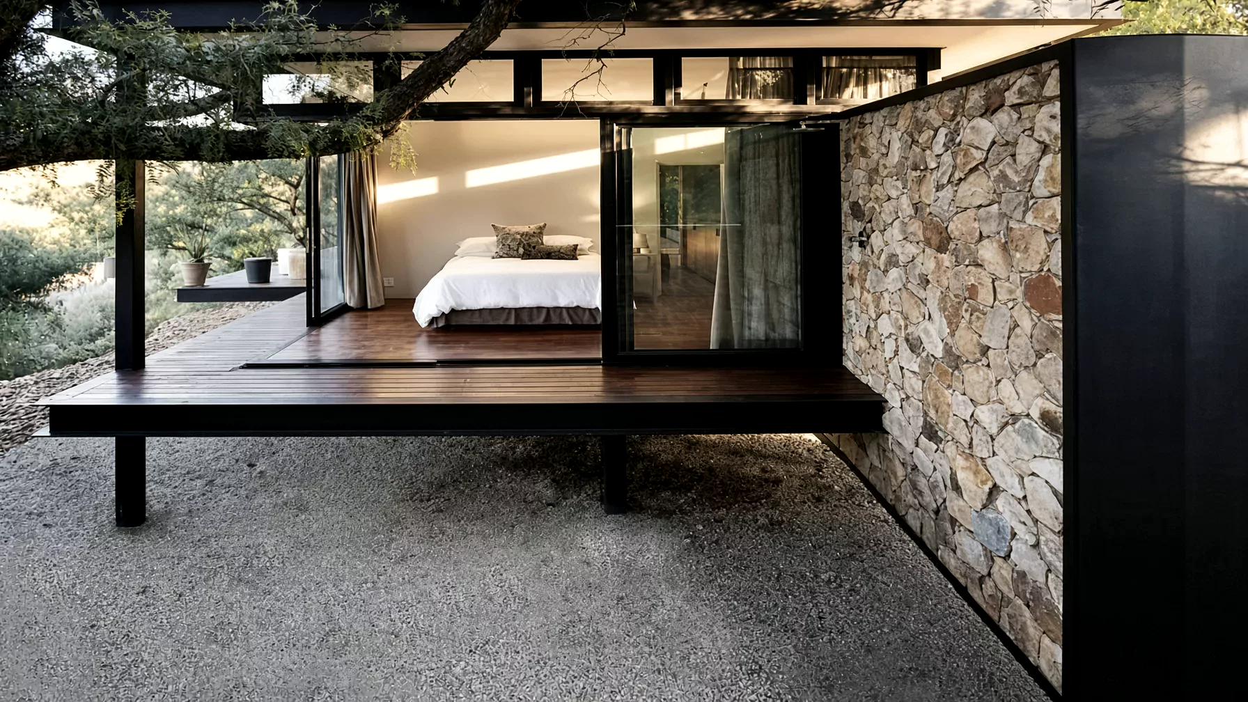A bedroom opening through glass doors onto a dark timber deck beside a stone wall