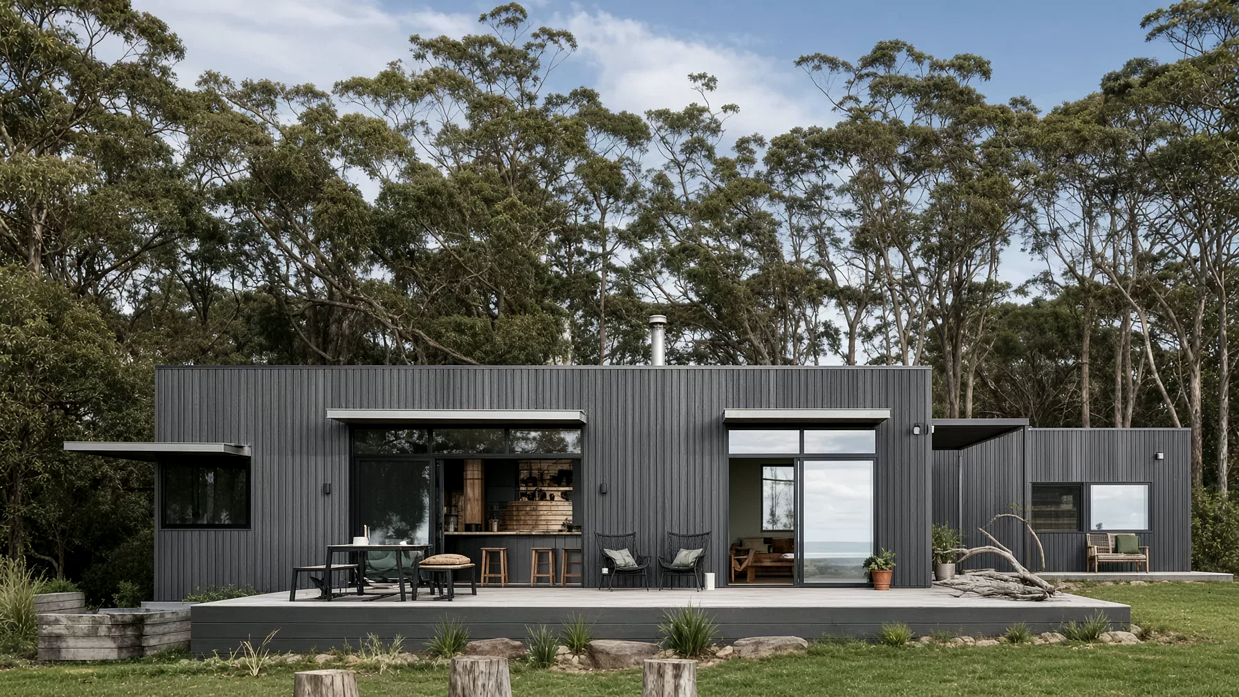 A dark clad single-storey cabin with a deep veranda and an outdoor kitchen